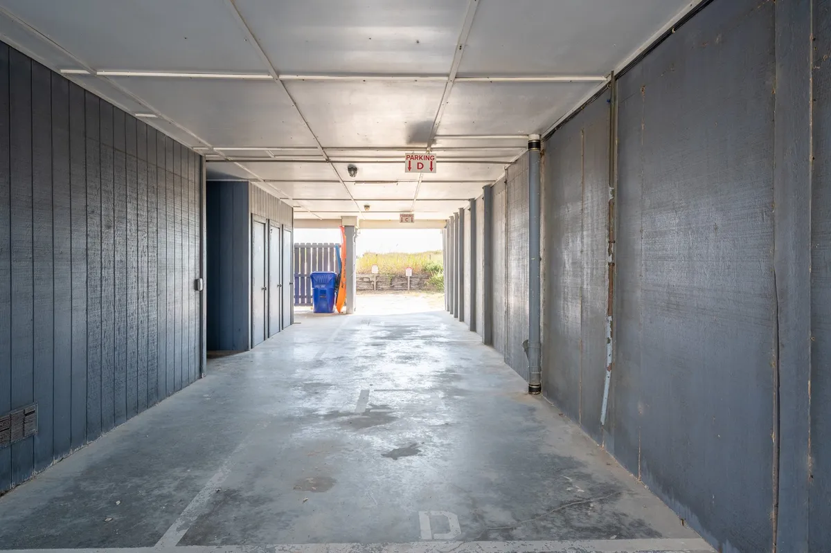 A long, well-lit corridor with blue accents, a trash bin, and clear exit signage—likely depicting the interior stairwell or shared hallway leading to the units. The scene feels organized and safe, suggesting easy access to residences from parking or entry points.