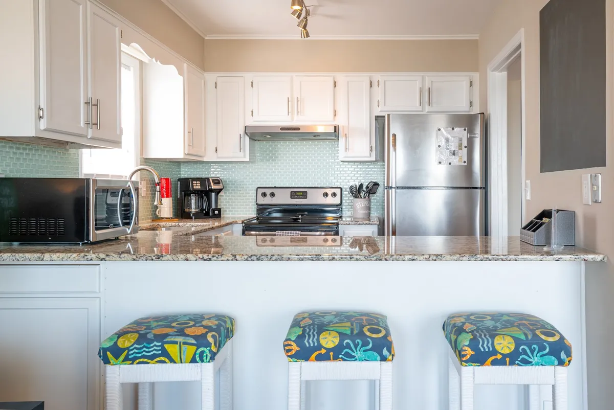 A welcoming kitchen interior featuring granite countertops, colorful bar stools, and stainless steel appliances. The scene is cheerful and lively, suggesting a perfect spot for casual dining, preparing meals together, or sharing snacks at the kitchen bar.