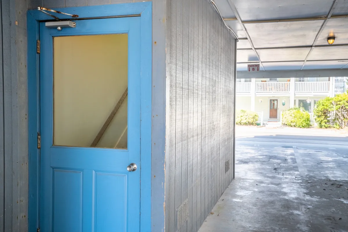 This image captures a blue door partially open with light streaming through, highlighting a textured wall and evoking a sense of entry and anticipation. The scene suggests a transition from the inside toward new experiences and possibilities.