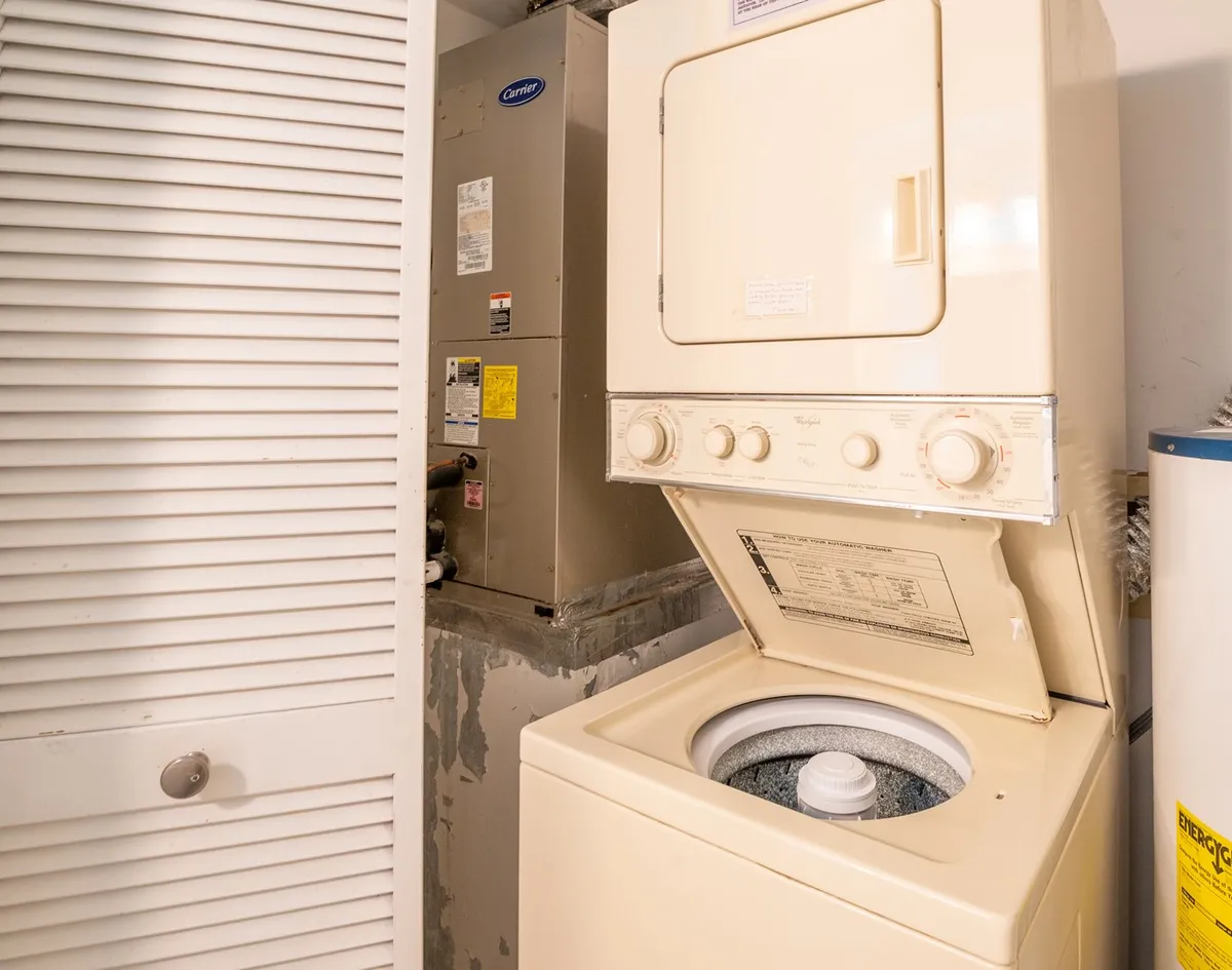 An interior close-up of a utility closet housing a stacked washer-dryer unit and water heater. The space is functional and clearly dedicated to in-unit laundry, emphasizing convenience for guests and families.